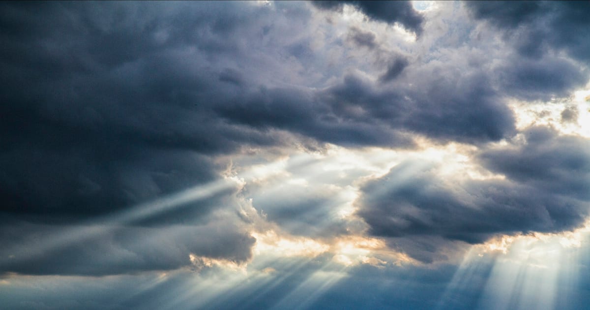 Shafts of sunlight breaking through a heavy bank of grey storm cloud