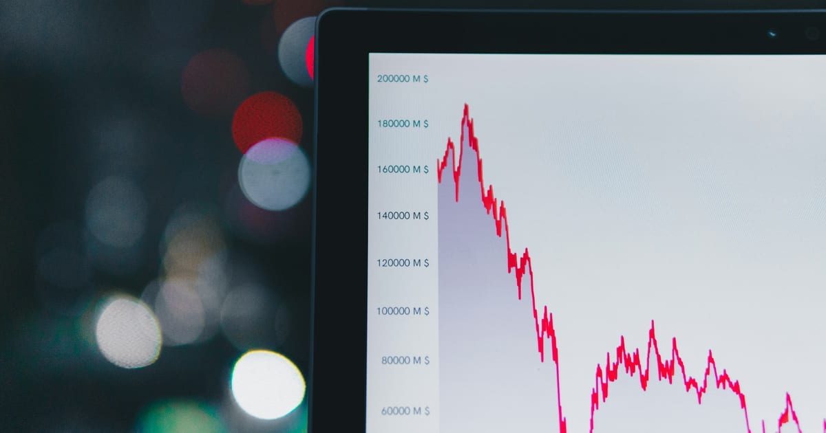 A screen showing a red price line falling steeply, with out-of-focus lights behind it